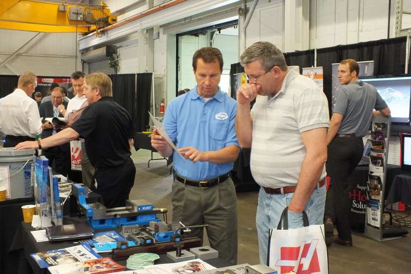 Mark Rodrigues, president of Machining ROI, a factory rep for Kurt vises, speaks with Danny Milicevic, of EQMS at the supplier tabletop area at the open house